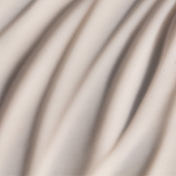 Creamy, pale surface with subtle wavy folds beside Odacité Retinol Therapy Hand Cream with PHA + Peptides tube.