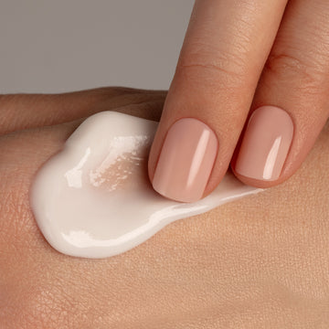 A hand with nude nails applies Odacité Retinol Therapy Renewing Hand Cream to another hand against a plain background.