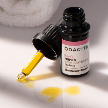 Odacite Bl+C Pimples Serum Concentrate bottle with yellow liquid spilled on a towel, for pimple-prone skin.