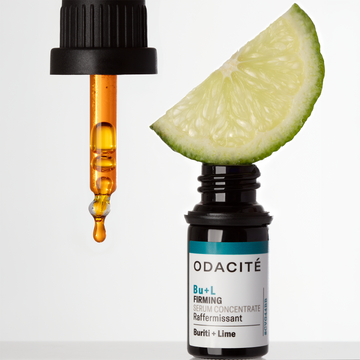 Dropper with orange serum and a lime wedge placed above Odacité Structural Reset Duo bottles on a plain background.
