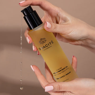 Hand holds Odacité Vitamin C & Retinol Targeted Body Essentials oil; liquid drips from pump against a plain background.