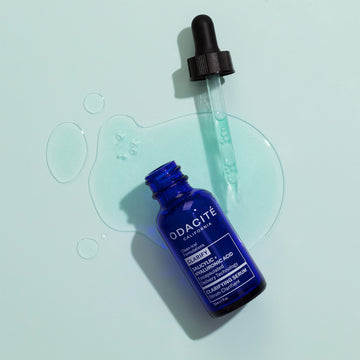 Odacité Clarifying Serum Salicylic + Hyaluronic Acid bottle with dropper on light blue background, next to drops of clear liquid.