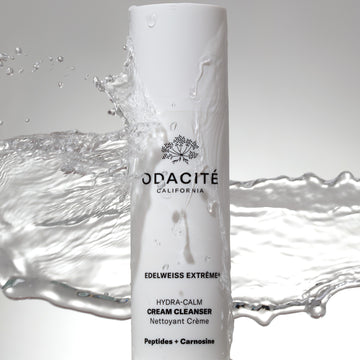 Odacité Daily Calm Cleansing Duo bottle with water splashing around it, highlighting the product’s liquid formula and packaging.