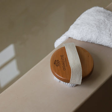 Odacité Dry Spa Brush with soft bristles on a folded white towel next to a bathtub, designed for sensitive skin.