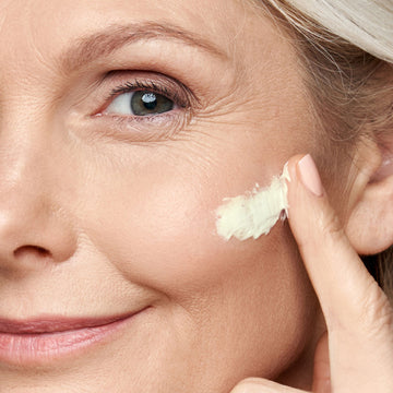 Older woman smiles while applying Odacité Bioactive Renew Supreme Cream • Edelweiss Extrême® • Peptides + Carnosine to her cheek.