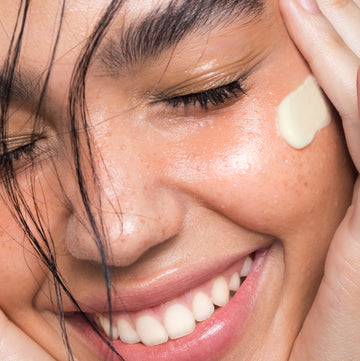 Person with closed eyes applies Odacité Day & Night Eye Care Duo to eye area, showing smooth skin and a gentle smile.