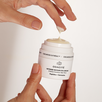 A hand dispenses Odacité Intense Repair Eye Cream • Edelweiss Extrême® from a white jar onto a fingertip.