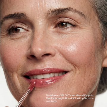A woman smiles while applying Odacité Glow More + Age Less Duo to her face. The bottles are visible in her hand.