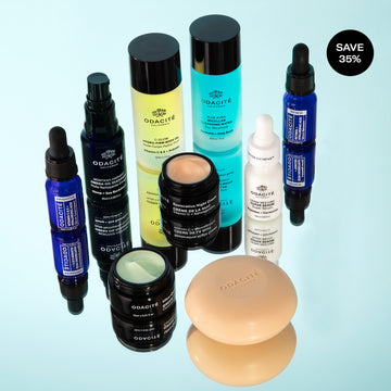 Odacité Luxe Experience serums, creams, and bars arranged on a reflective light blue surface.