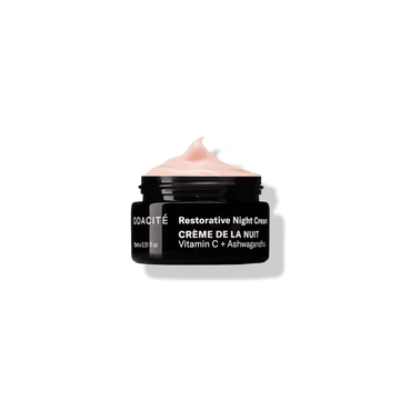 Black jar of Odacite Crème de la Nuit Vitamin C + Ashwagandha Restorative Night Cream with pink cream, on a white background.
