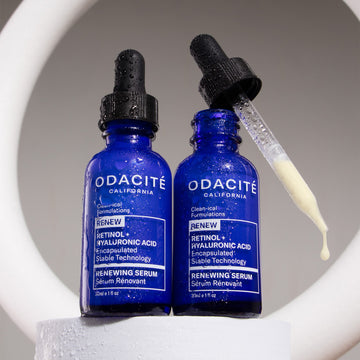 Two blue Odacité bottles on a white background; one is open with a yellow drop of Renewing Serum • Retinol + Hyaluronic Acid.