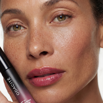 Woman with radiant skin holds a tube of Odacité SPF 40 Nourishing Lip Serum close to her face.