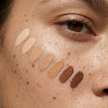 Six Odacité Glow More + Age Less Duo swatches in varying tones are applied to a person’s cheek for comparison.