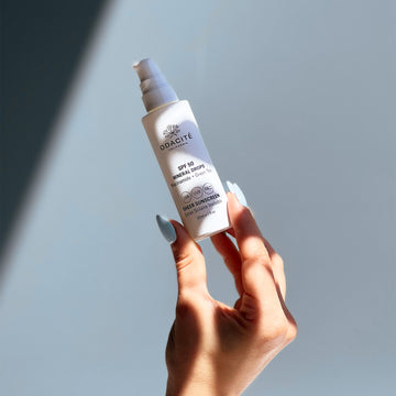 Hand holding Odacité Mineral Drops SPF 50 Sheer Sunscreen with Niacinamide + Green Tea against a softly lit background.