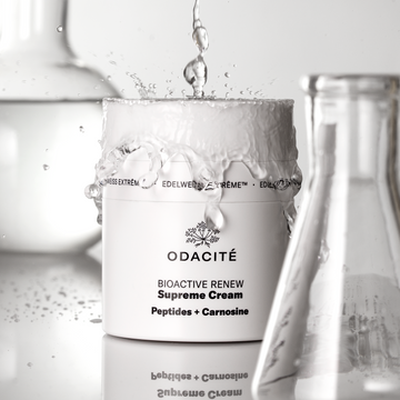 Odacité Structural Reset Duo (Supreme Cream & Bu+L) jar with water splashes and clear glass beakers, shown for skin barrier care.