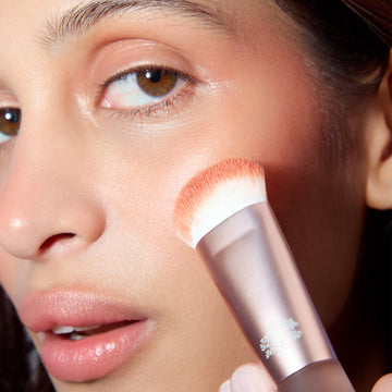 Hand holding the Odacité Universal Brush applies pigment to cheeks, blending for a smooth, natural finish.