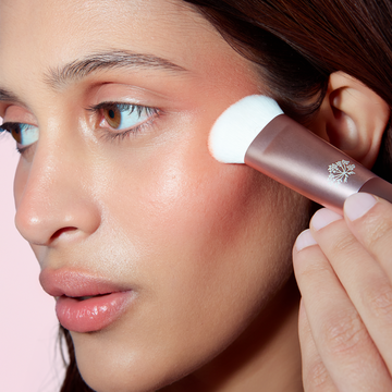 Woman applies makeup with the Odacité Universal Brush, blending pigment on her smooth, glowing skin.