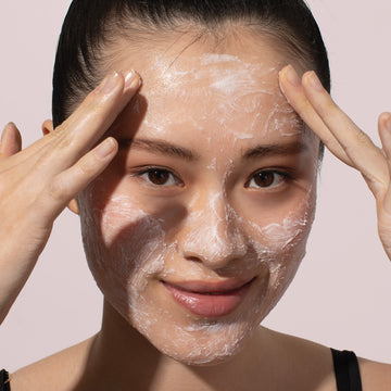 Woman massages Odacité Jojoba Pearls + White & Rooibos Tea Daily Hydra-Exfoliant onto her face, smiling gently.