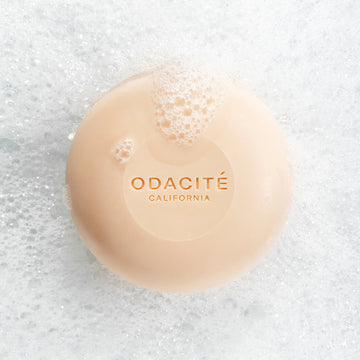 Odacite 552M Argan + Coconut Soap Free Shampoo Bar with bubbles sits on thick white foam and suds.