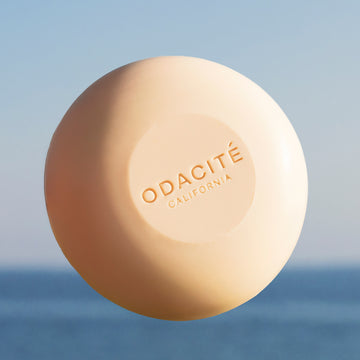 Odacité 552M Argan + Coconut soap-free shampoo bar, beige, on a surface with ocean and sky in the background.