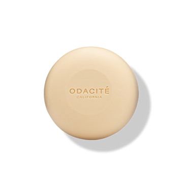 Round, beige ODACITÉ 552M Argan + Coconut Soap Free Shampoo Bar on a white background with a soft shadow.