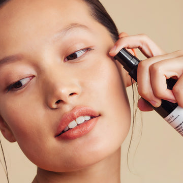 Woman applying Odacite All-Embracing Watermelon + Hibiscus Facial Oil, beige background.