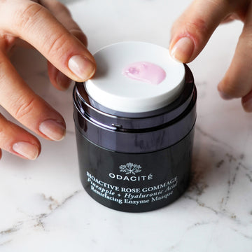 Hands opening Odacite Bioactive Rose Gommage mask jar; label lists pineapple, hyaluronic acid, and resurfacing enzymes.