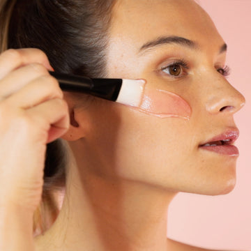 Woman uses a brush to apply Odacite Bioactive Rose Gommage, a creamy enzyme mask, on her face.