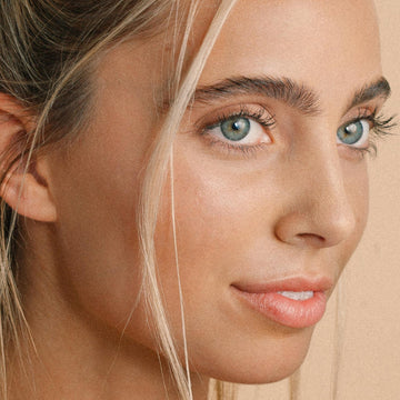 Young woman’s face shown close up, holding Odacite Ca+C Camelina + Chamomile Serum Concentrate for sensitive skin.