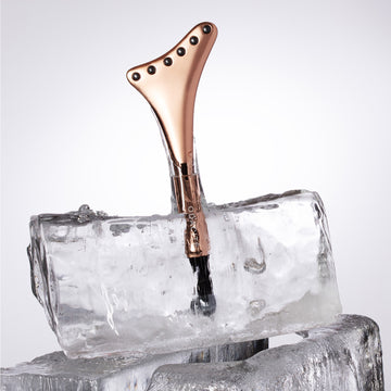The Odacité Cryo-Tech Facial Tool • Powered by Terahertz, rose gold with studs, rests in clear ice on a white background.