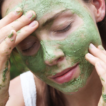 Woman with closed eyes applies Odacite Green Ceremony Cleanser, a green Matcha and Spirulina powder, to her face.