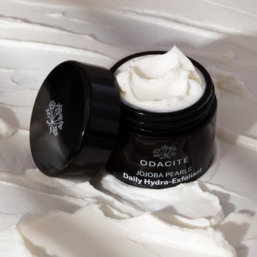 Odacité Jojoba Pearls White + Rooibos Tea Daily Hydra-Exfoliant open on textured cream background, showing white exfoliating cream.