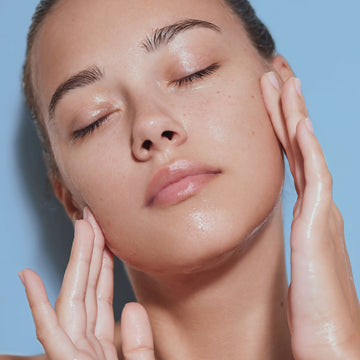 Person with eyes closed touches their glowing skin after applying Odacite le Blue Balm with Blue Chamomile & Shea Butter repair balm.