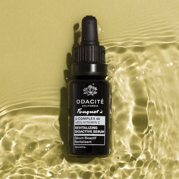 Odacité Le Complex 46 Revitalizing Bioactive Serum bottle on rippled golden liquid background, labeled 15% Vitamin C.