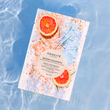 Odacite Mood Cleansing Bath Soak with Himalayan salt, grapefruit, and lemongrass floats above rippling water with colorful powders.